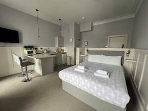 Una habitación de hotel moderna con una cama, un escritorio, un microondas, un lavabo y un televisor.