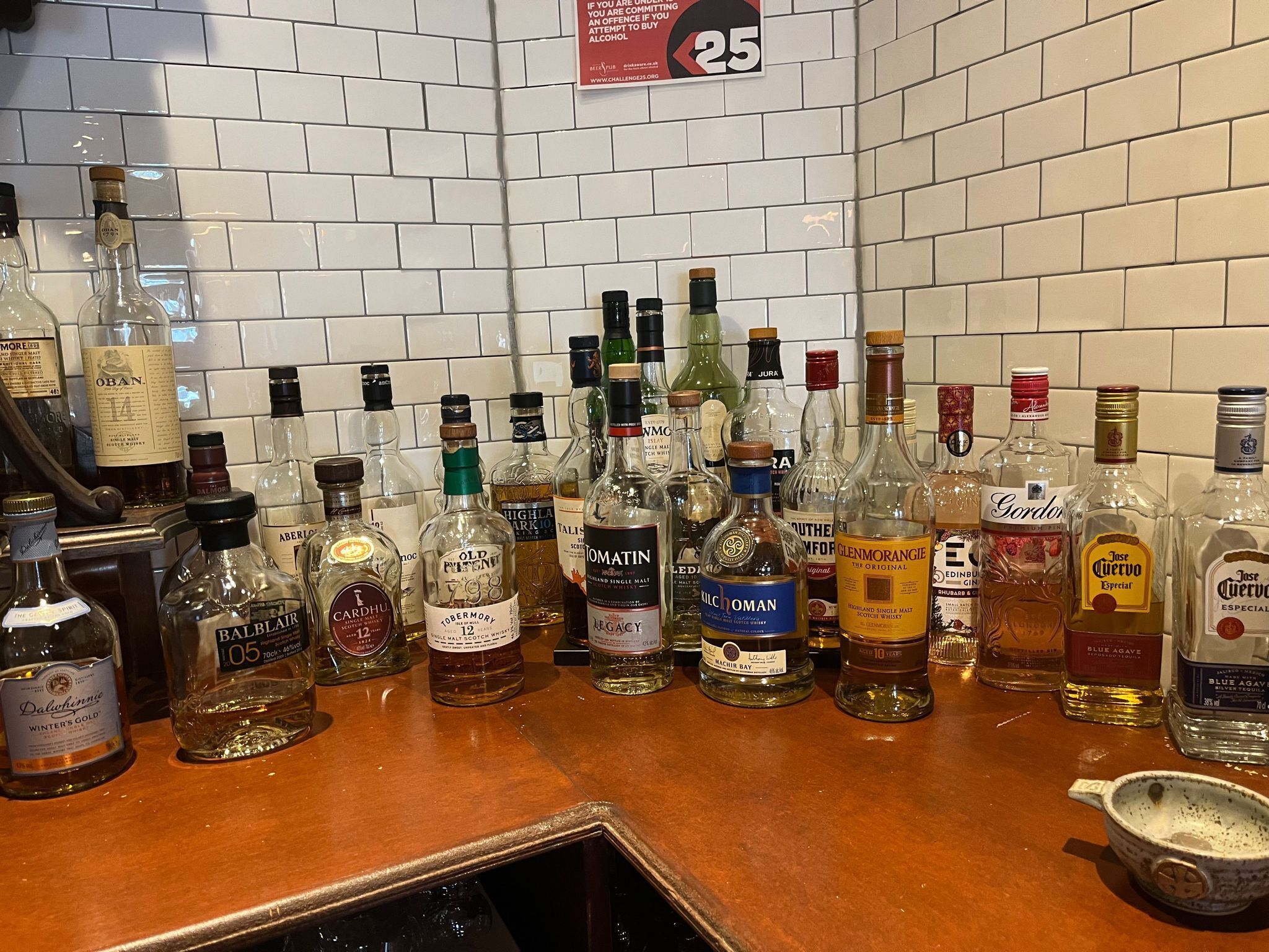 A bar counter with various bottles of alcohol, including whisky and gin, against a tiled wall.