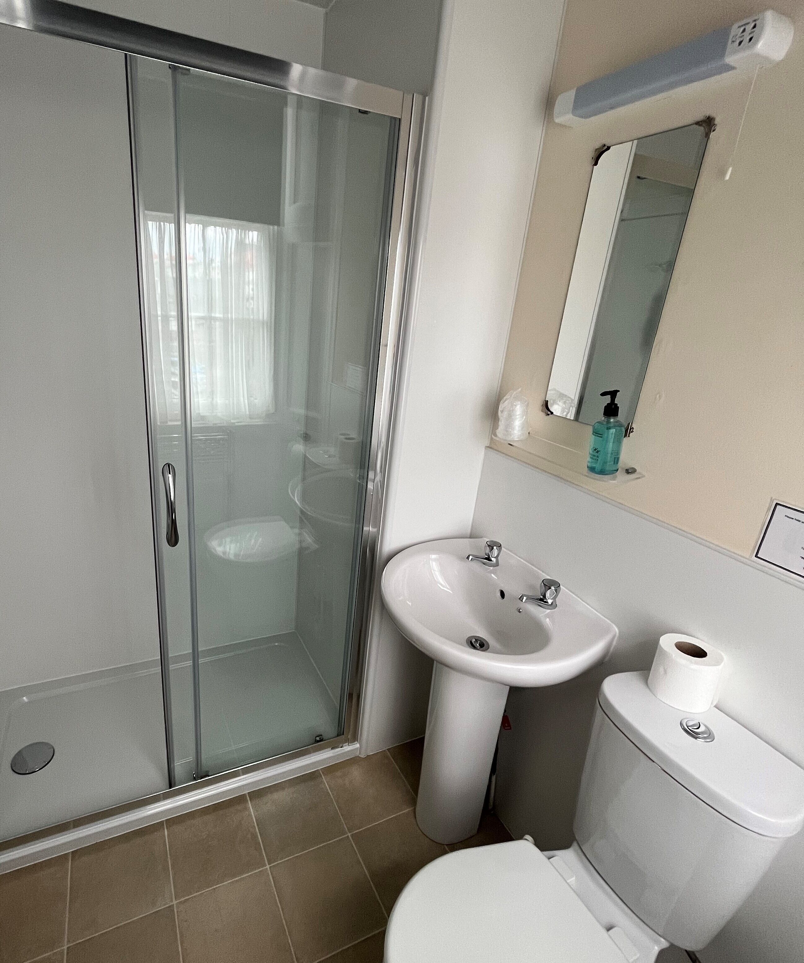 A bathroom with a glass shower enclosure, a white sink, a mirror, and a toilet.