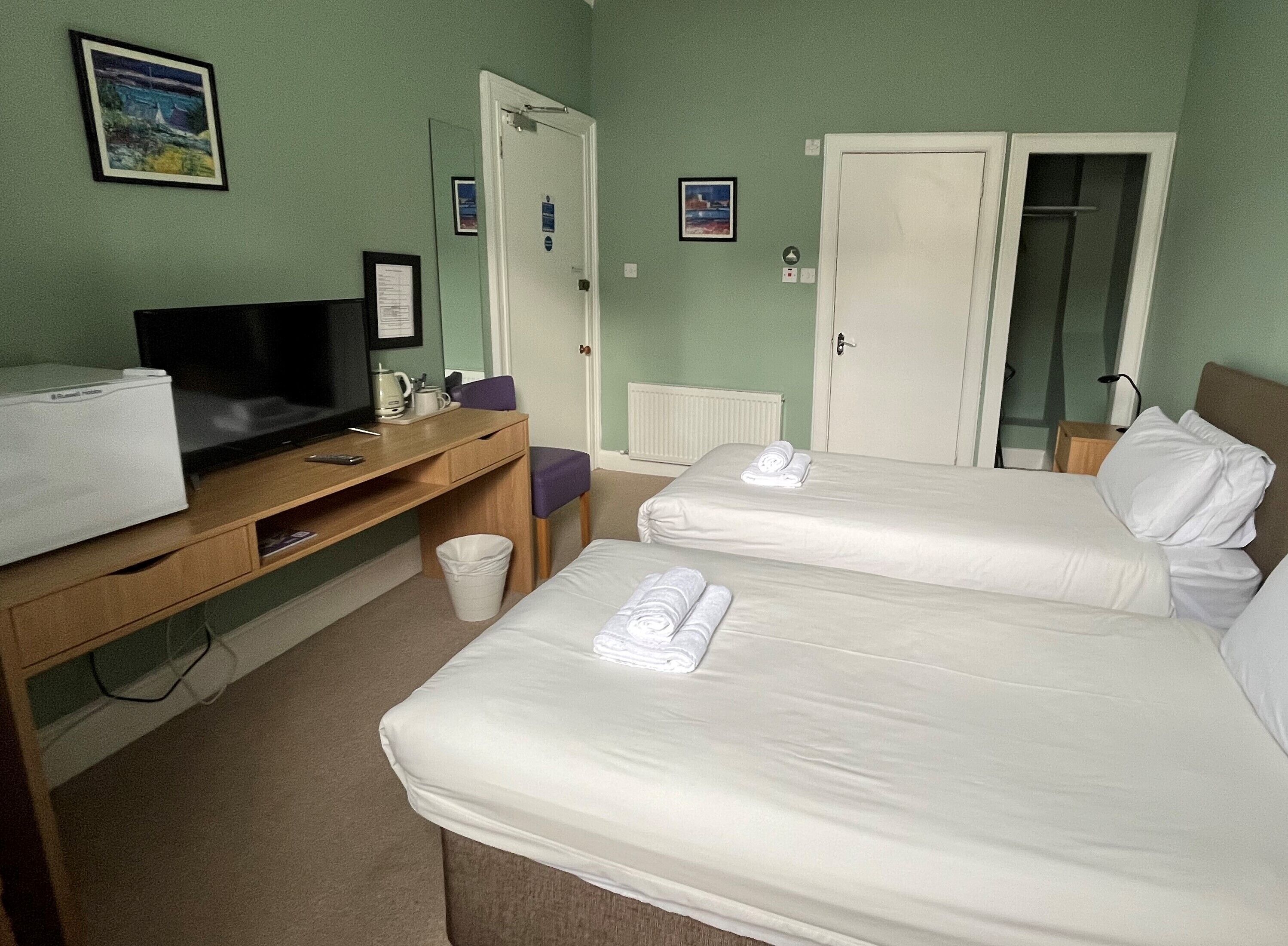Una habitación de hotel con dos camas, un escritorio con televisor y un cesto de basura pequeño.