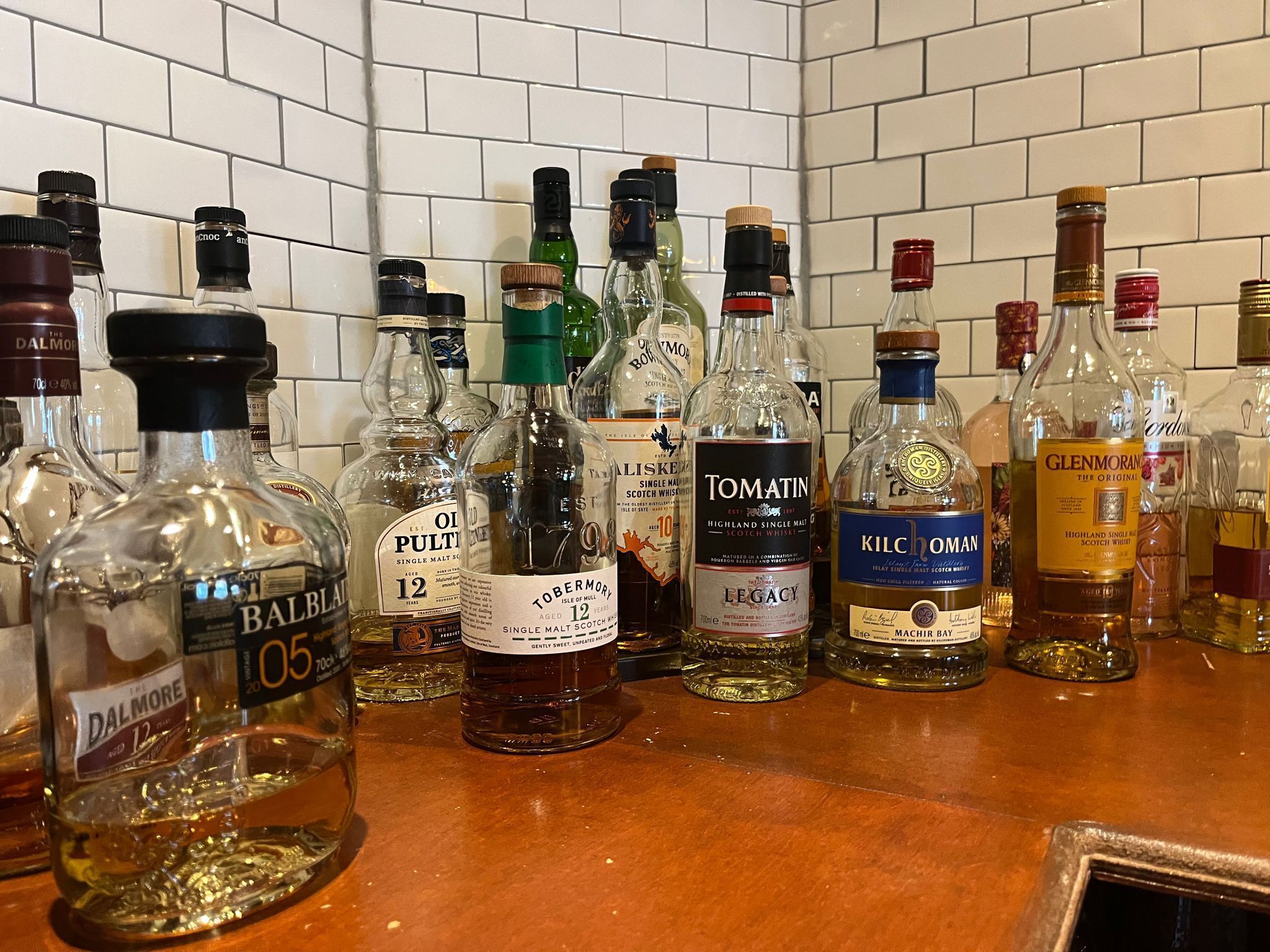 Variedad de botellas de whisky sobre una barra con salpicadero de azulejos.