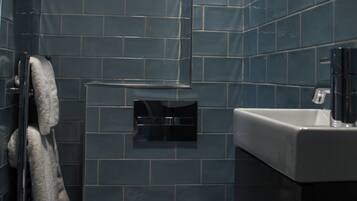 A bathroom with two toilets, a sink, a towel rack, and a trash bin.