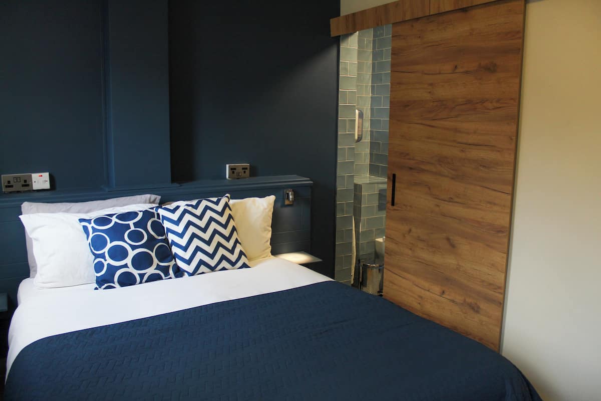 Un lit bien fait, avec un oreiller à motifs bleus et blancs, une tête de lit en bois et un mur recouvert de carreaux.