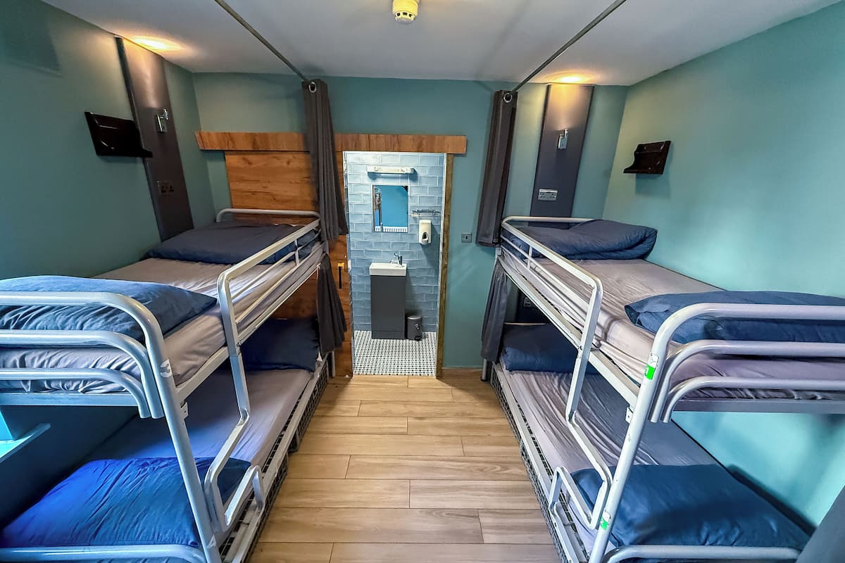 Une pièce de taille modeste avec des lits superposés, une petite salle de bain dotée d’un miroir et une cloison en bois.