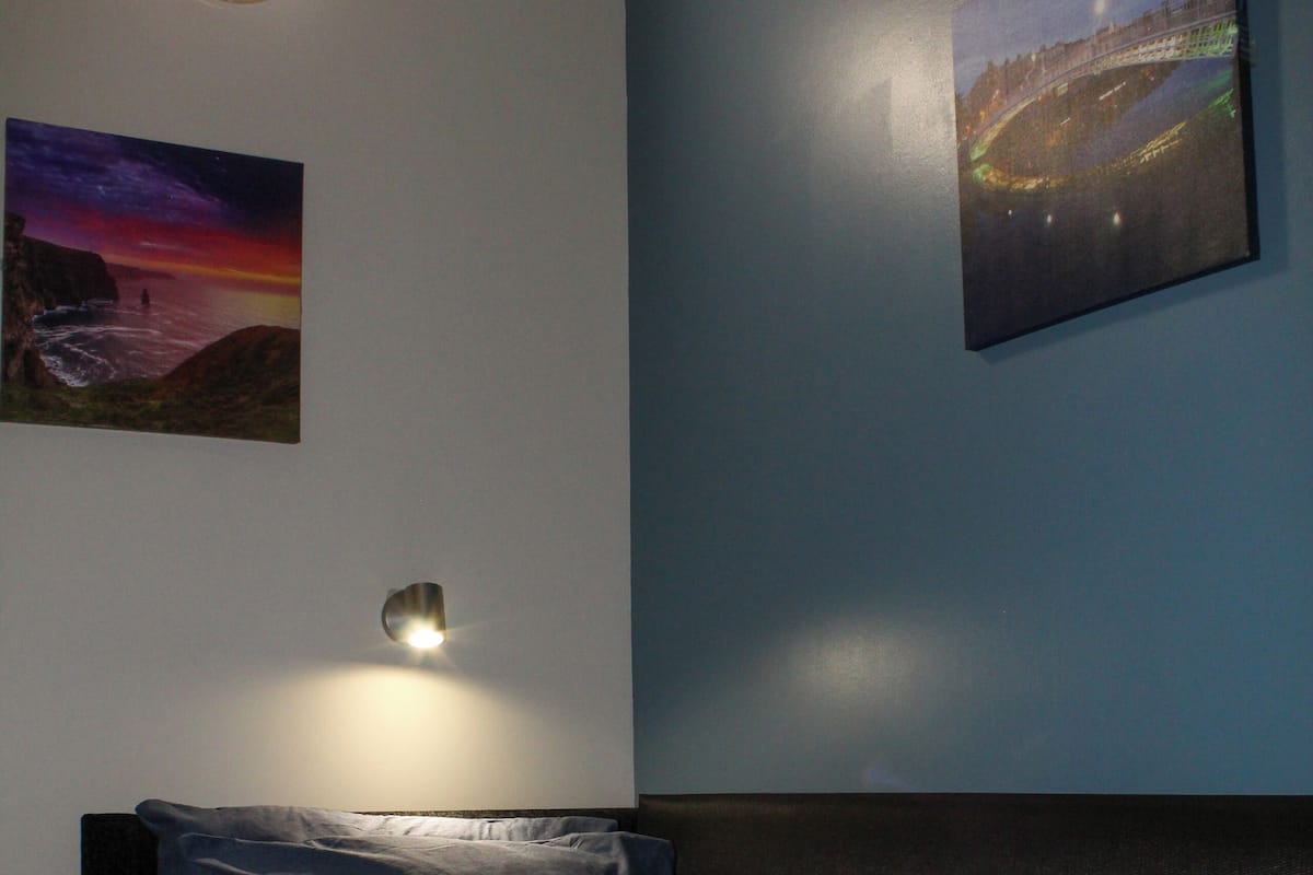 Une chambre à coucher avec un lit, des oreillers, une table de chevet et des œuvres d’art murales.