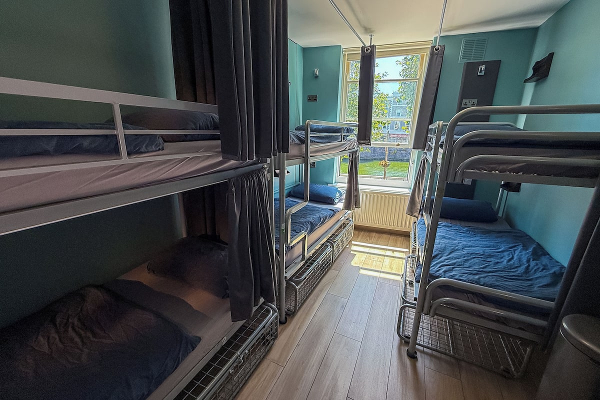 Une chambre avec plusieurs lits superposés, une fenêtre avec des rideaux et un radiateur.