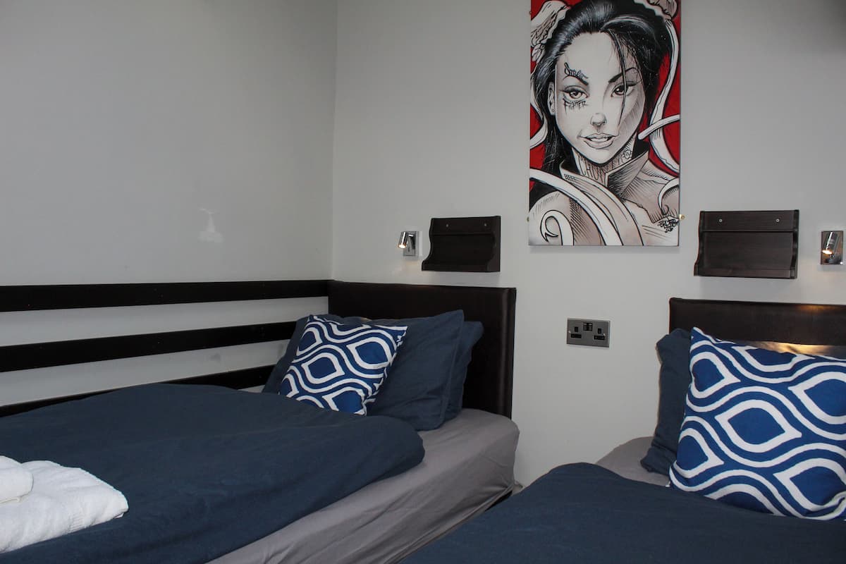 Une chambre d’hôtel avec deux lits, chacun orné d’un oreiller à motifs bleus et blancs, une serviette blanche sur le lit de gauche et une œuvre d’art accrochée au mur au-dessus des lits.