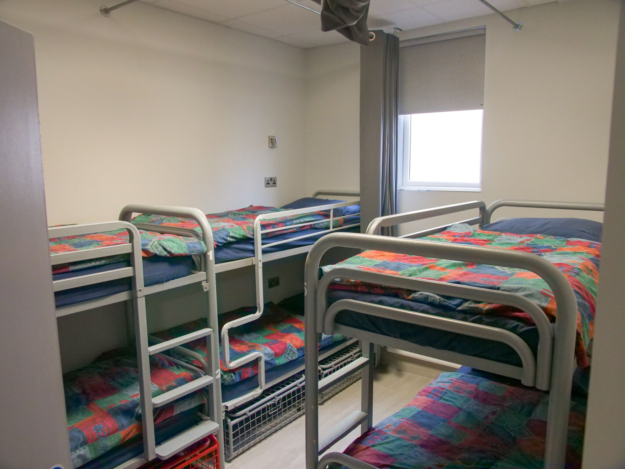 A dormitory room with bunk beds, a window, and a door.