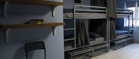 A dormitory room with bunk beds, a chair, shelves, and a window.
