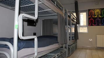A dormitory room with bunk beds, a window with a view, and a colorful Buddha painting on the wall.