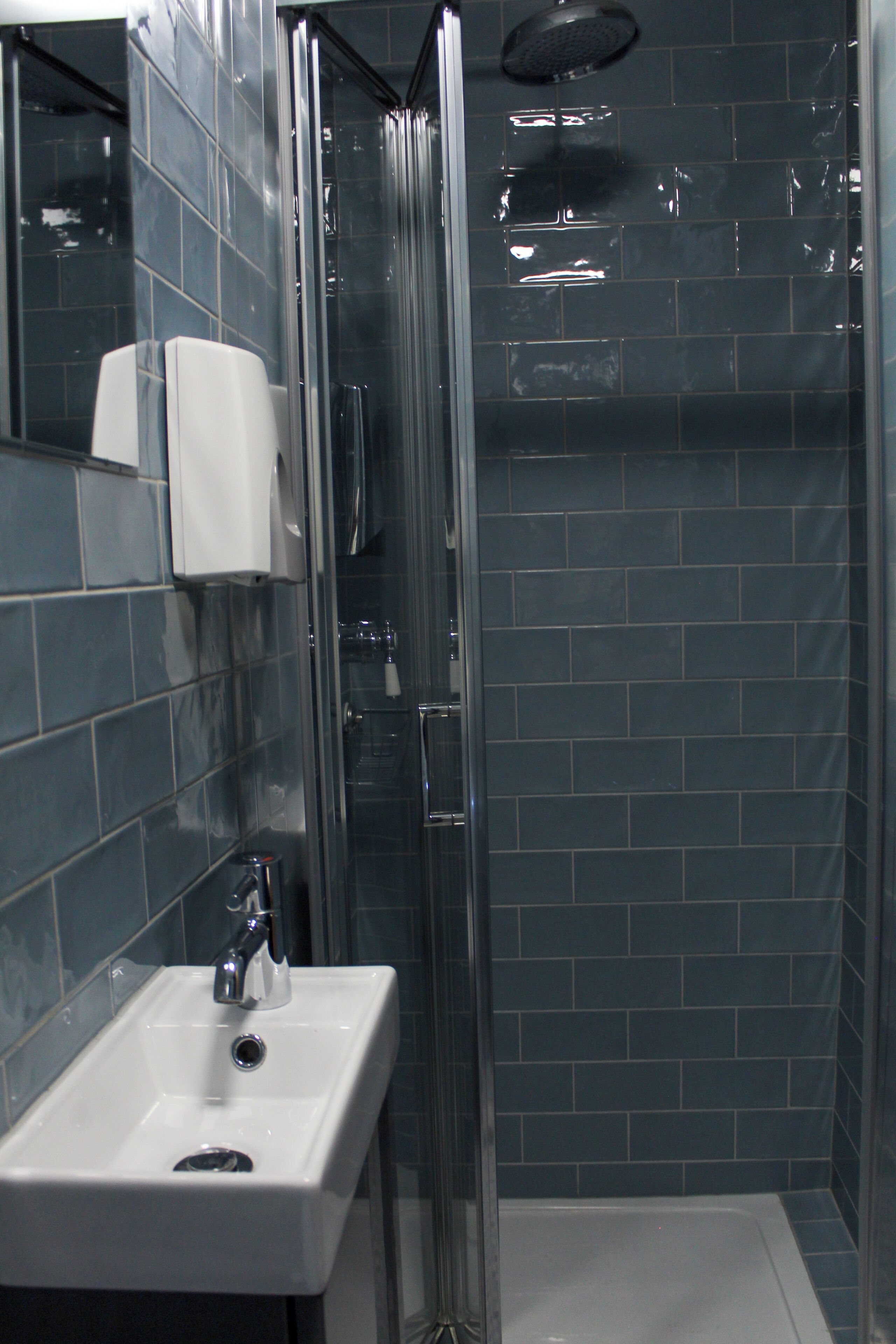 A modern bathroom with a glass-enclosed shower, a white sink, and a hand soap dispenser.
