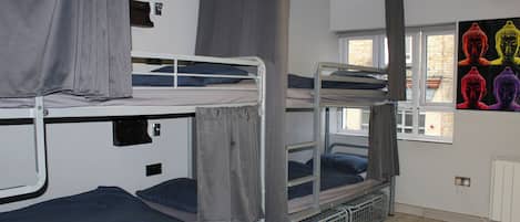 A dormitory room with bunk beds, a window with curtains, and a wall with Buddha statues.