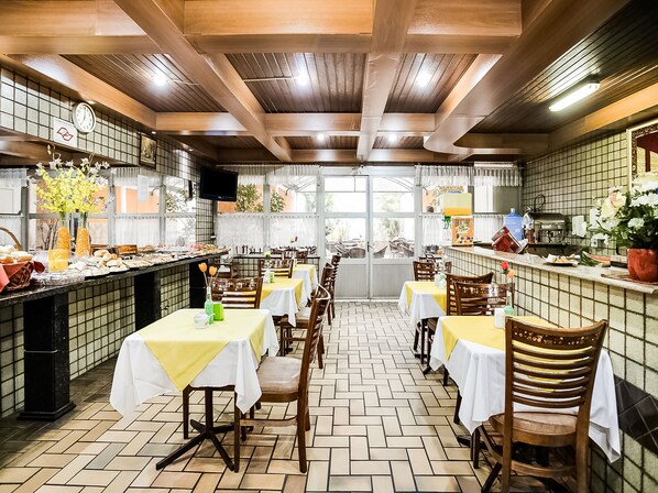 Un restaurante con varias mesas y sillas, una zona de cocina y un suelo de baldosas.