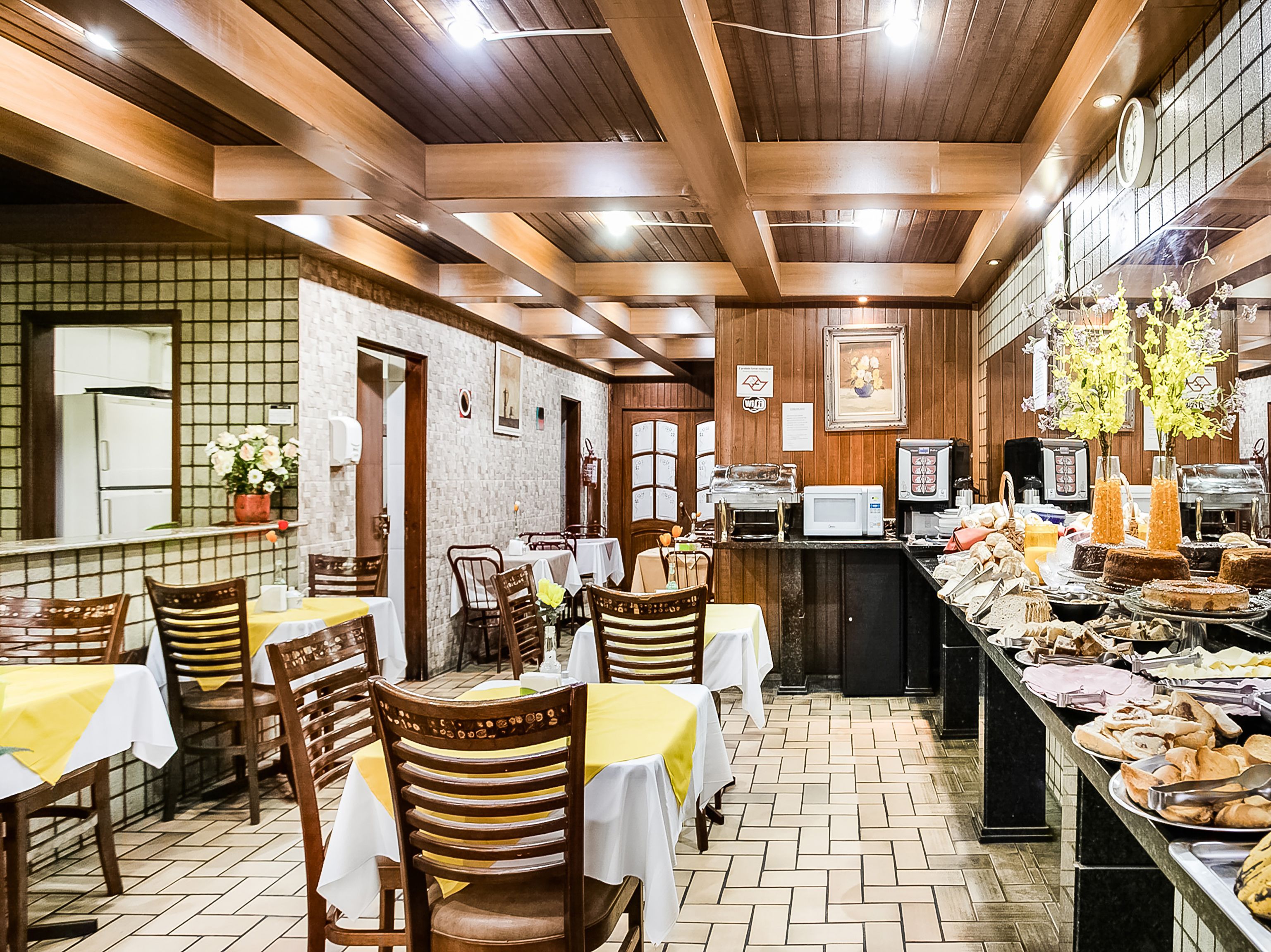 A restaurant with wooden ceiling beams, tiled floor, and tables set with white tablecloths.