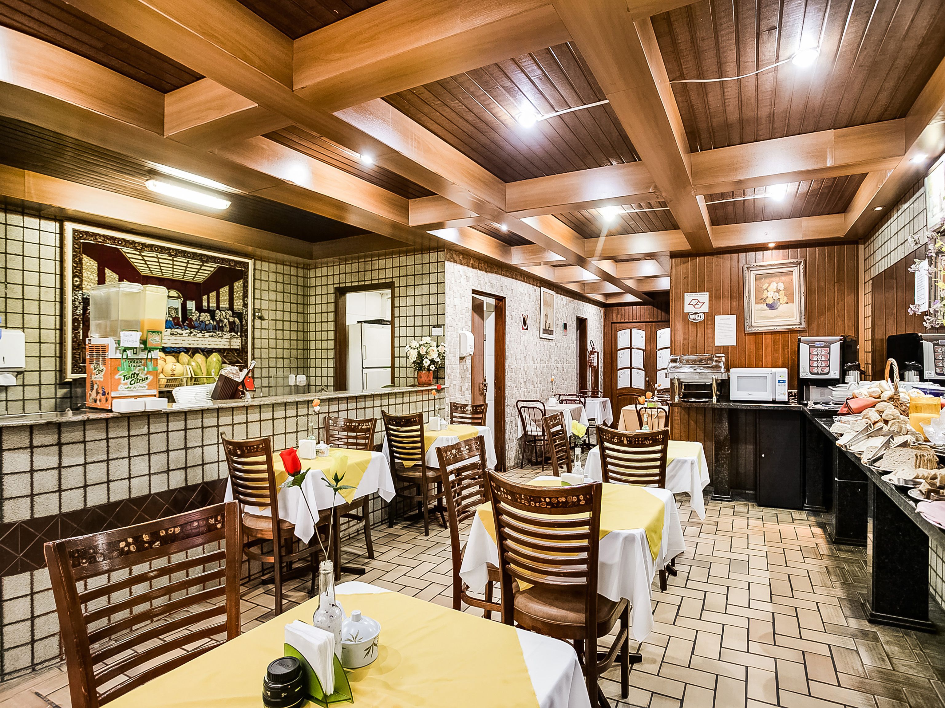 Un restaurant amb bigues de sostre de fusta, parets de rajola i taules cobertes amb camases blanques.