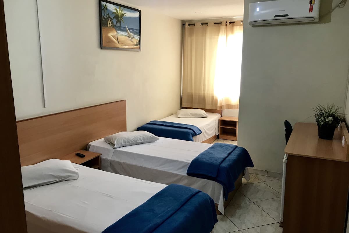 Ein Hotelzimmer mit zwei Betten, einem Schreibtisch, einem Stuhl, einem kleinen Tisch, einer Topfpflanze und einer Klimaanlage.