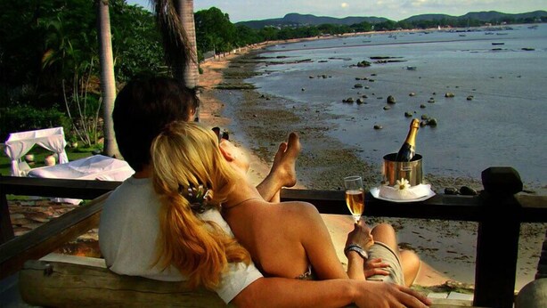 A couple sitting on a wooden bench overlooking a beach with palm trees and a view of the sea. - Pousada Martin Pescador (Búzios)