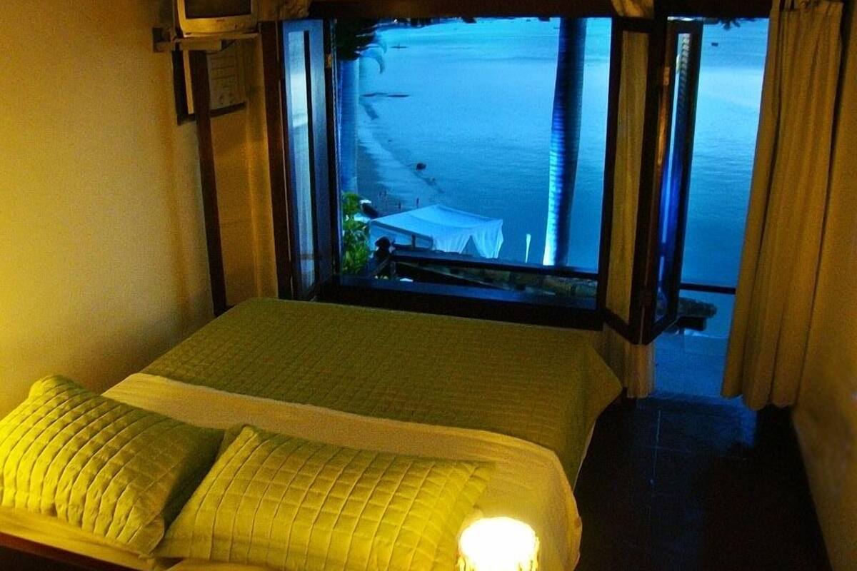 A bed with a view of the beach and ocean through an open window.