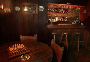 Una zona de bar con paredes de madera, un tablero de ajedrez sobre la mesa y taburetes.