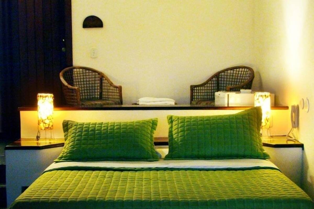 A hotel room with a bed, two nightstands, two lamps, and two wicker chairs.