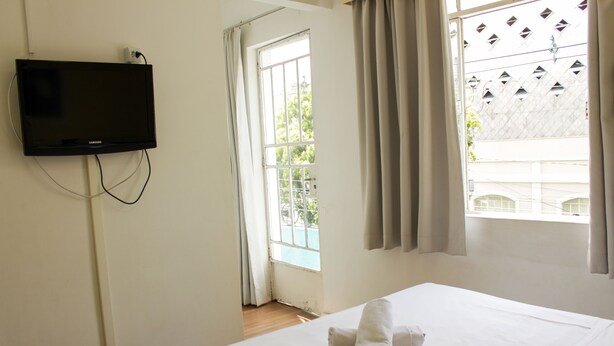 A hotel room with a bed, a TV mounted on the wall, and a window with curtains.