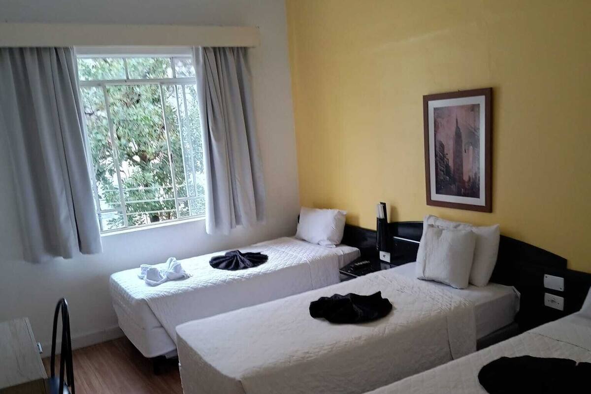 A hotel room with two single beds, a window with curtains, a painting on the wall, and a wooden floor.