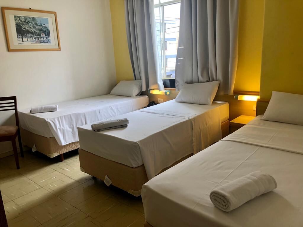 A hotel room with three single beds, a chair, a desk, and a window with curtains.