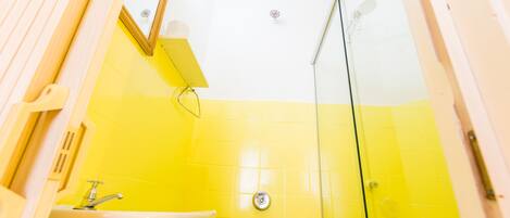 Un baño con pared de azulejos amarillos, un lavamanos blanco y un espejo.