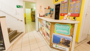 A hotel reception area with a counter, a staircase, and a corridor leading to other rooms.