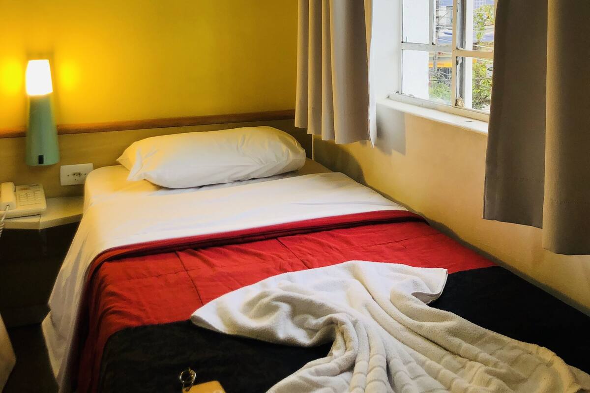 A hotel room with a bed, a nightstand with a lamp, and a window with curtains.