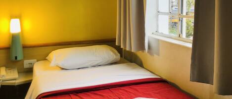 A hotel room with a bed, a nightstand with a lamp, and a window with curtains.