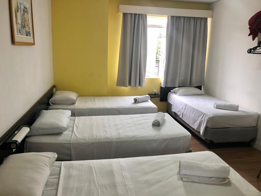 A hotel room with three single beds, a window with curtains, and a framed picture on the wall.