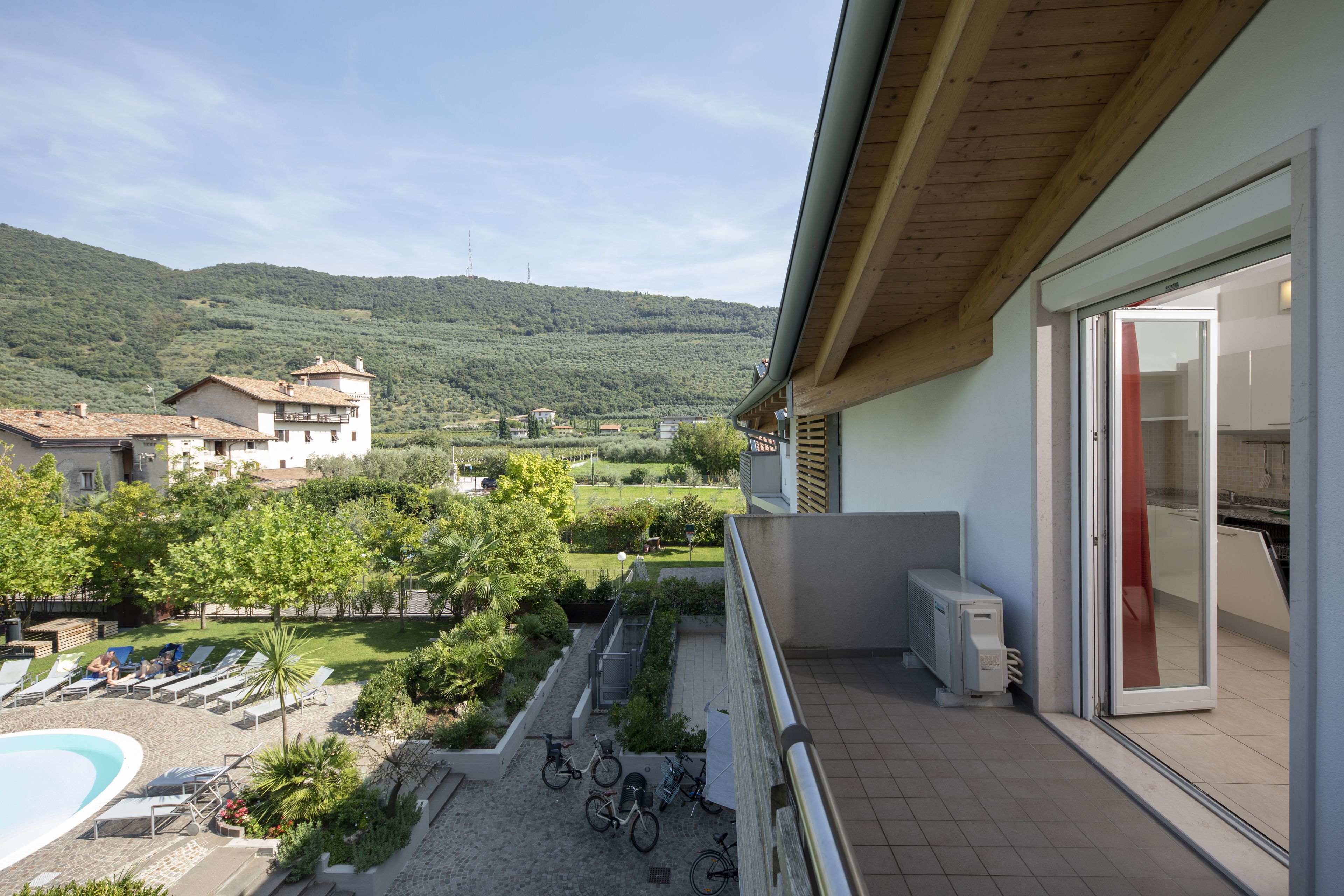 A balcony with a view of a swimming pool, bicycles, and a lush green landscape.