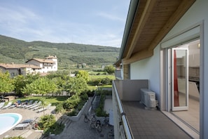 A balcony with a view of a swimming pool, bicycles, and a lush green landscape.