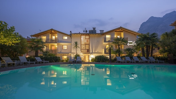 A hotel with a swimming pool, multiple balconies, and a mountain backdrop.
