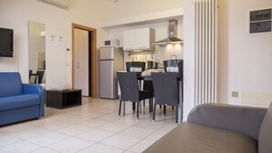 A compact living space with a kitchenette, a dining area with four chairs, a sofa, and a TV mounted on the wall.