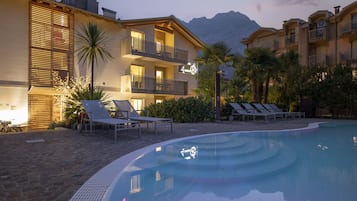 A hotel with a swimming pool, lounge chairs, and a mountain view.