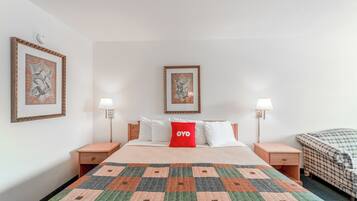 Habitación de hotel ordenada, con una cama grande, dos mesitas de noche, un cojín rojo y dos lámparas de pared.