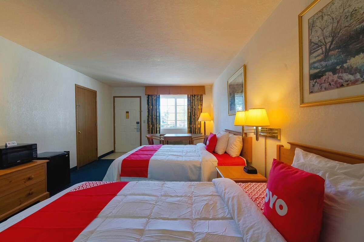 A hotel room with two beds, a desk, a chair, a microwave, and a door.