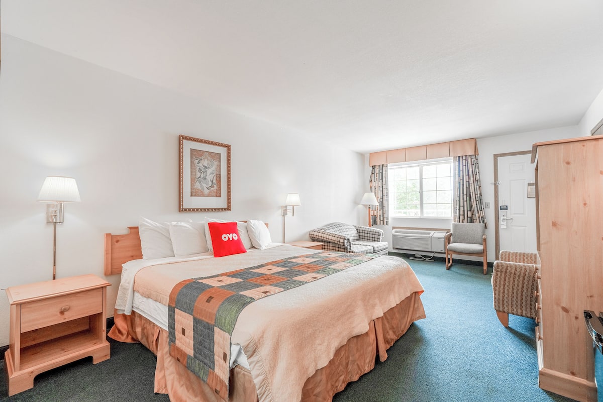 A hotel room with a large bed, a desk, a chair, and a wardrobe.