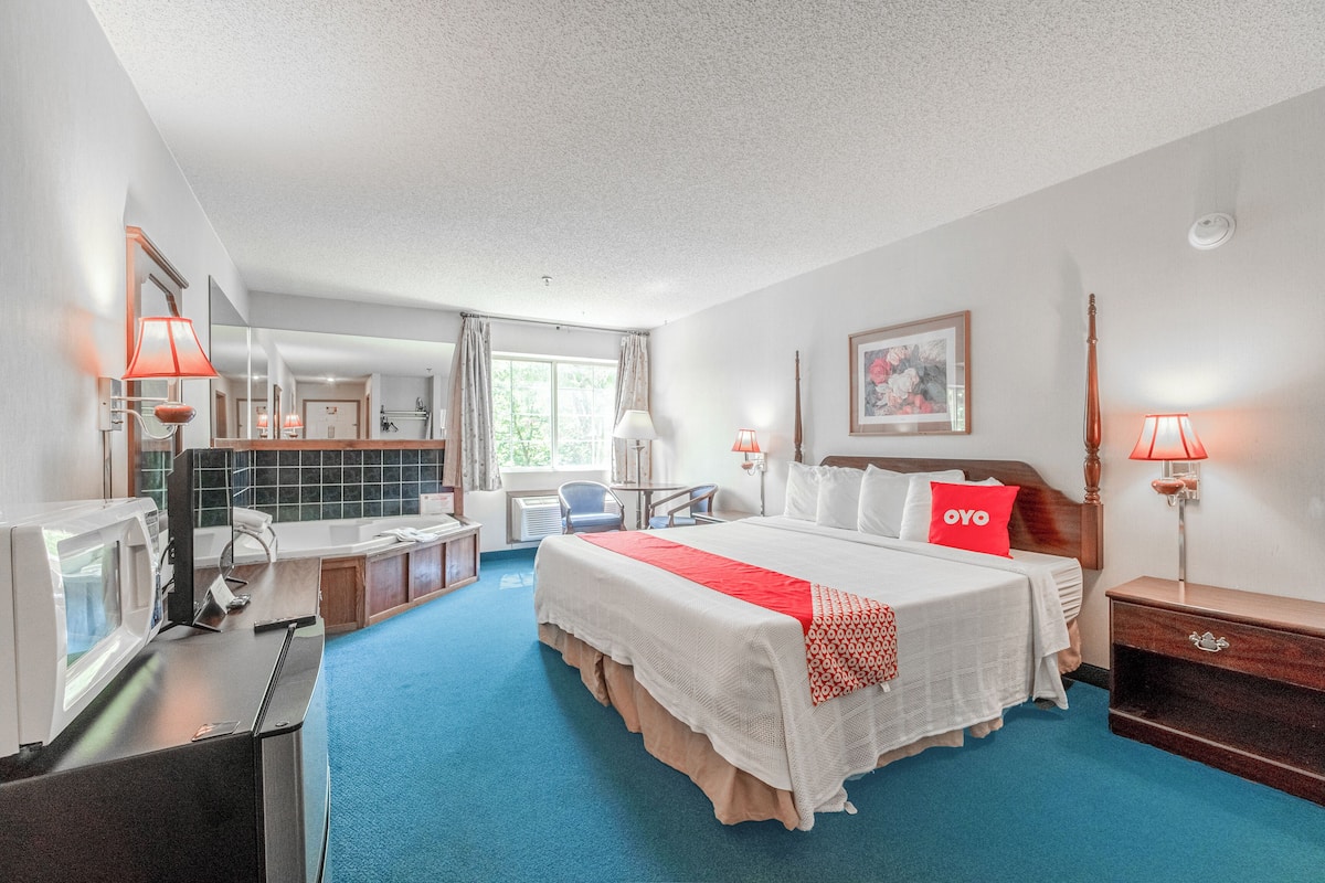 A hotel room with a large bed, a desk with a computer, a chair, a window with curtains, and a painting on the wall.