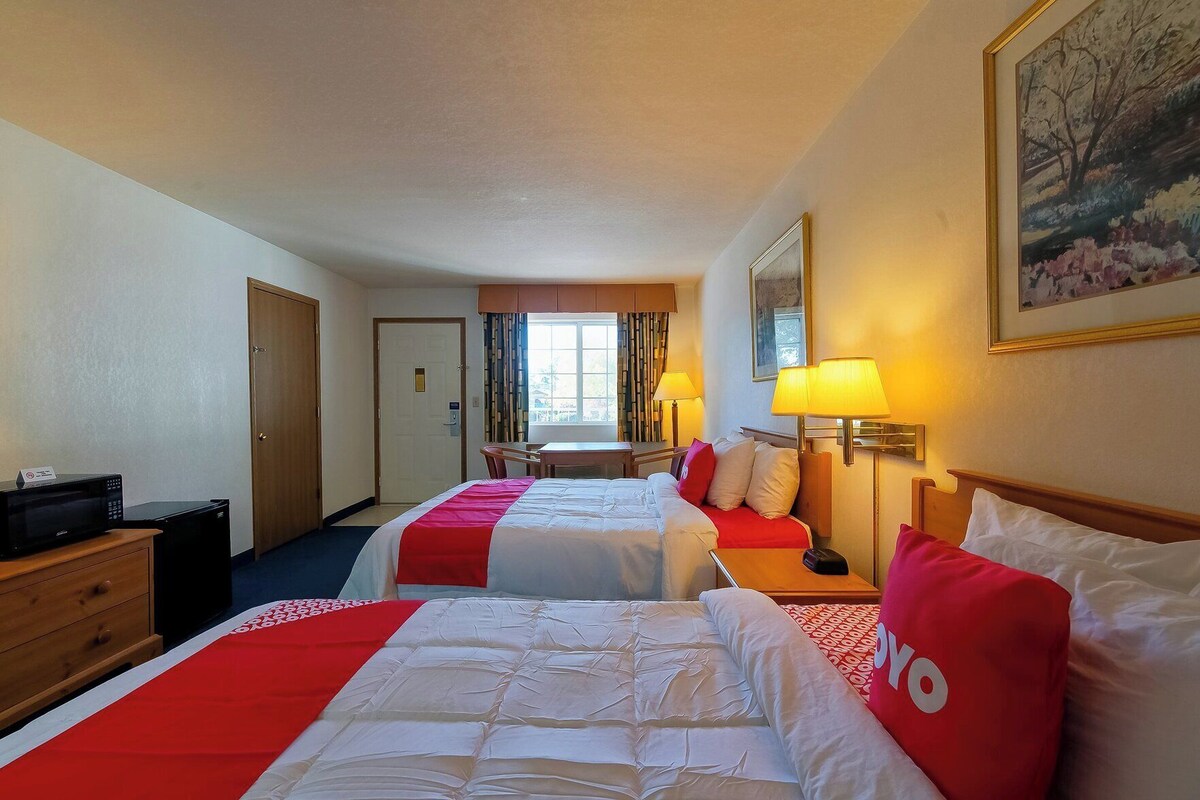 A hotel room with two beds, a desk, a chair, a microwave, and a TV.