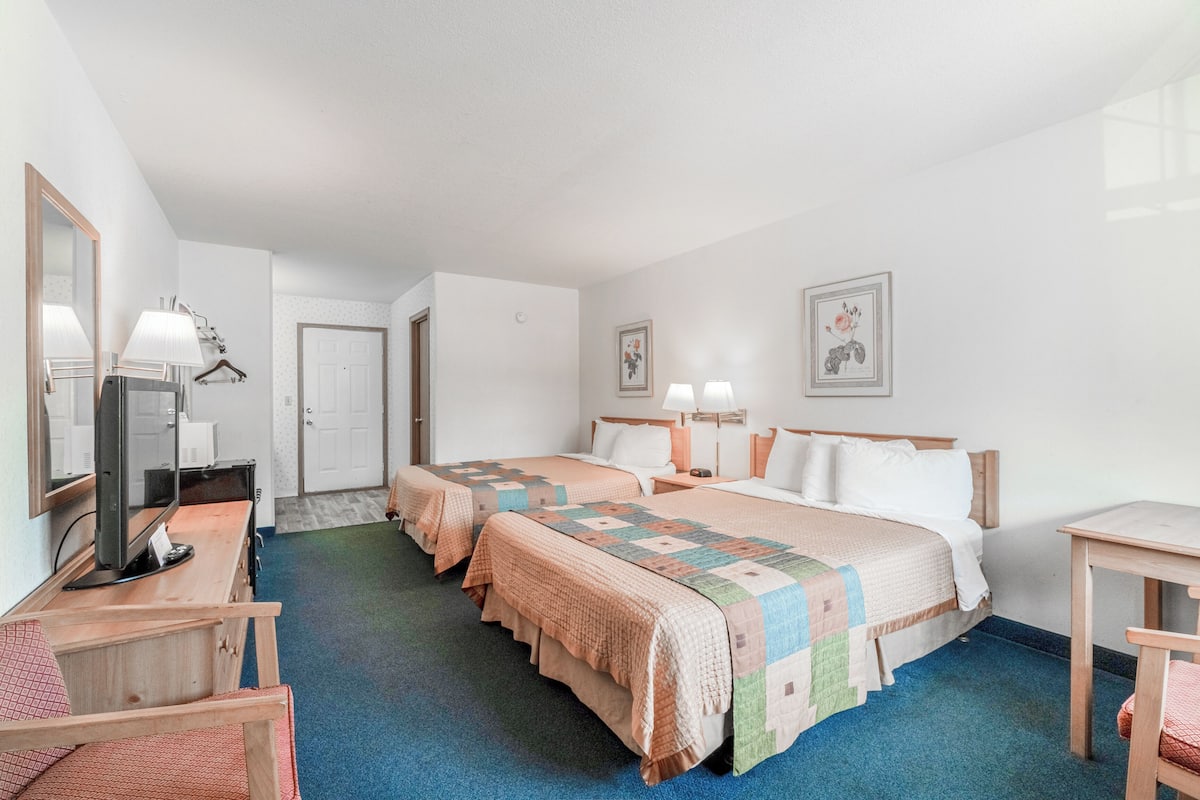 A hotel room with two beds, a desk with a computer, a chair, and a small table.
