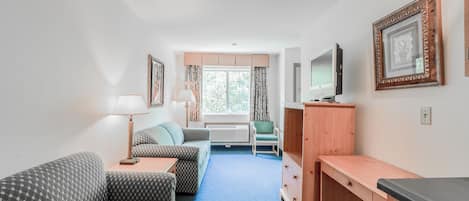 A compact room with a sofa, a desk, a television, and a window with curtains.