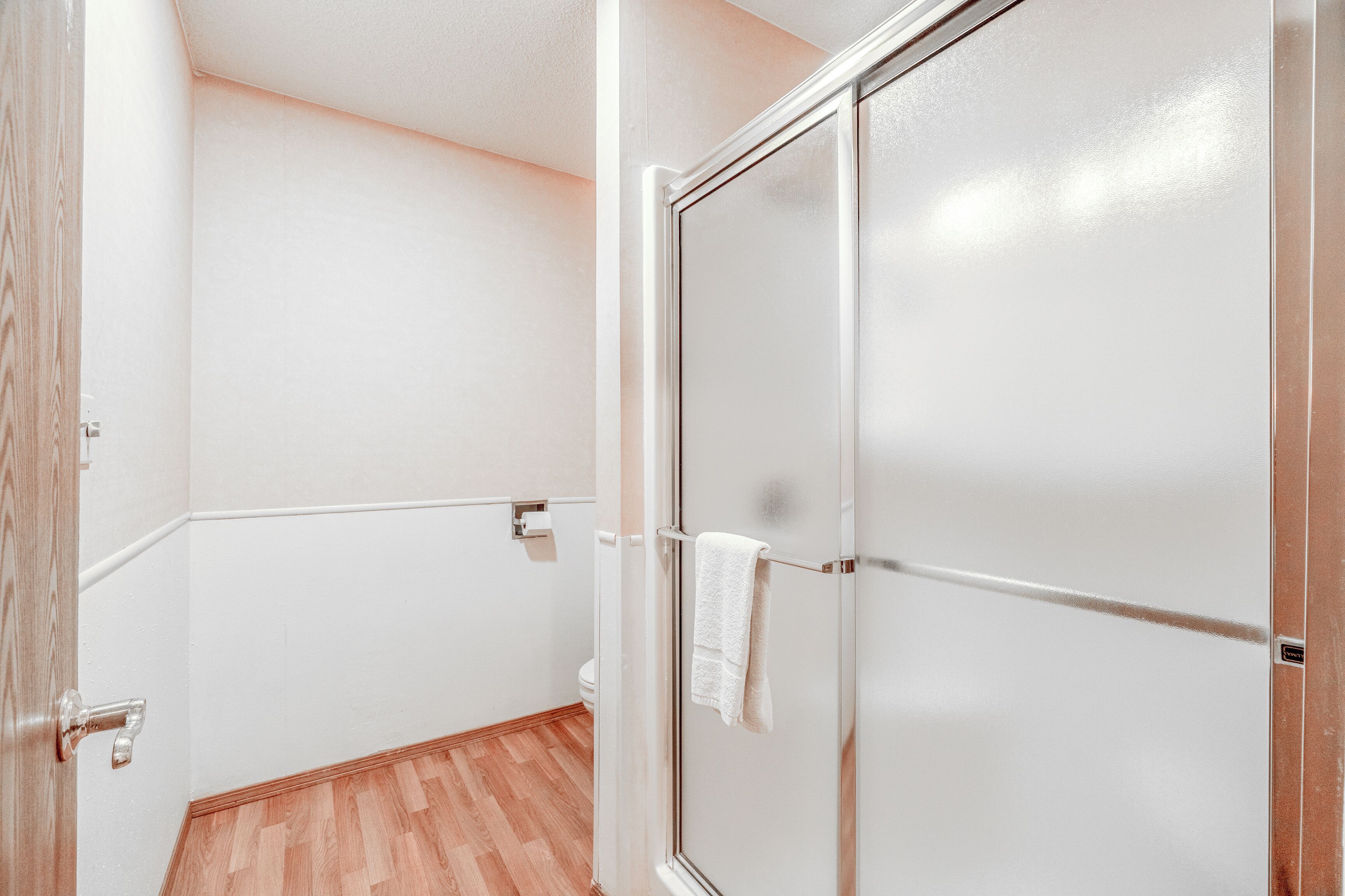 Een badkamer met een houten vloer, witte wanden en een glazen douchedeur.