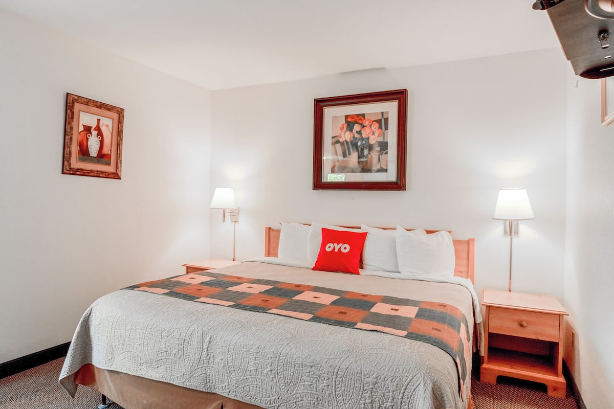 A hotel room with a bed, two bedside tables with lamps, a red pillow, and two framed pictures on the walls.