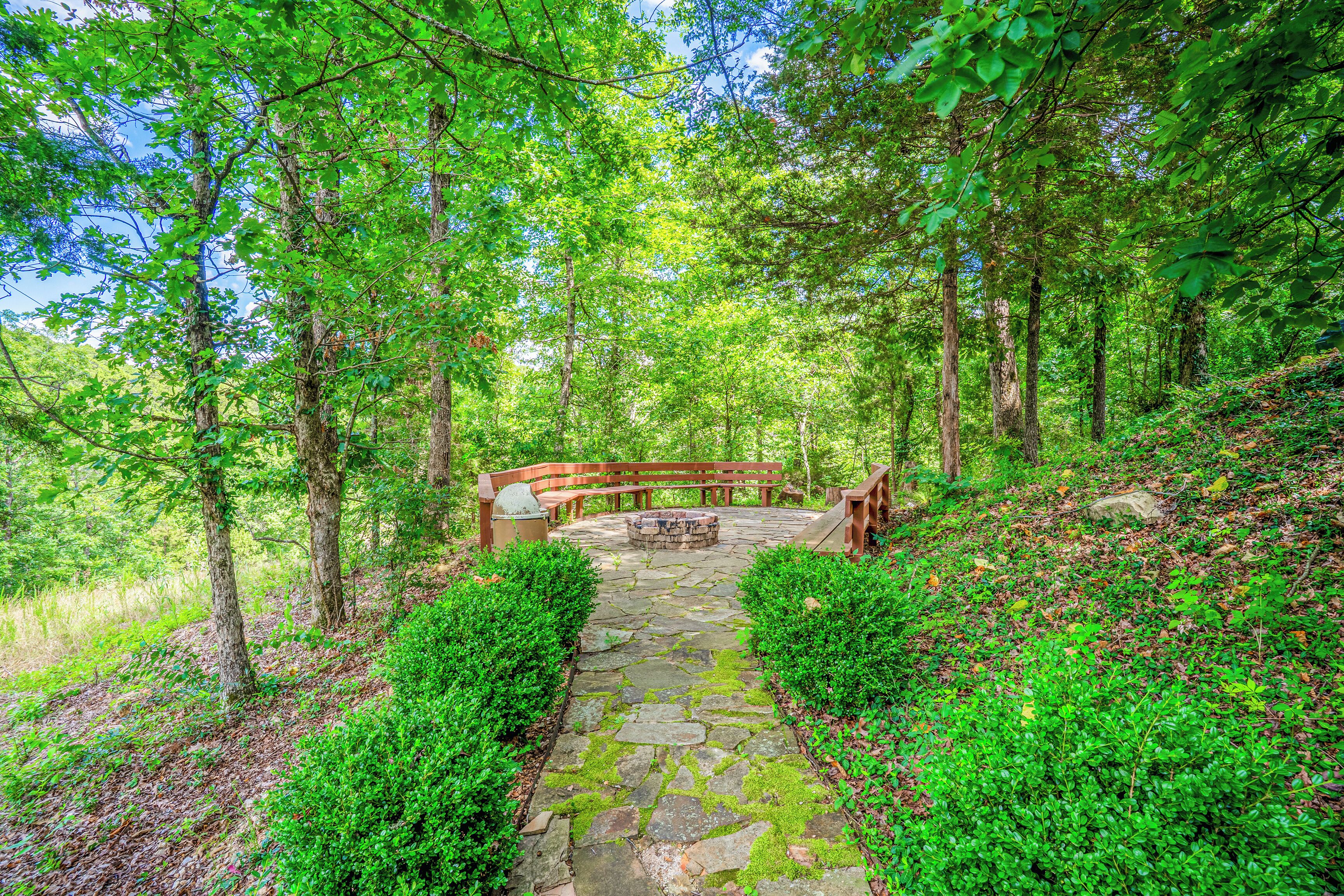 A stone pathway leading to a wooden bench and fire pit in a forested area.