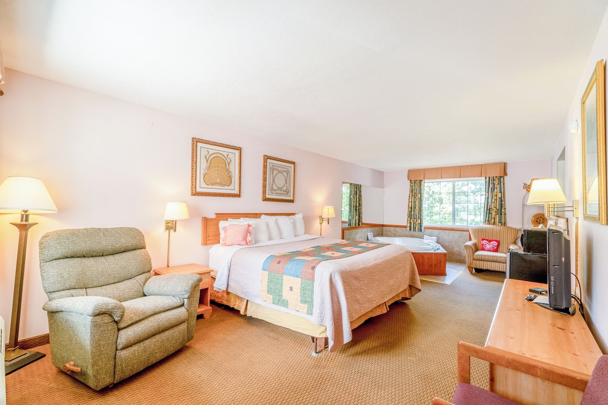 A hotel room with a bed, a chair, a desk, and a computer.