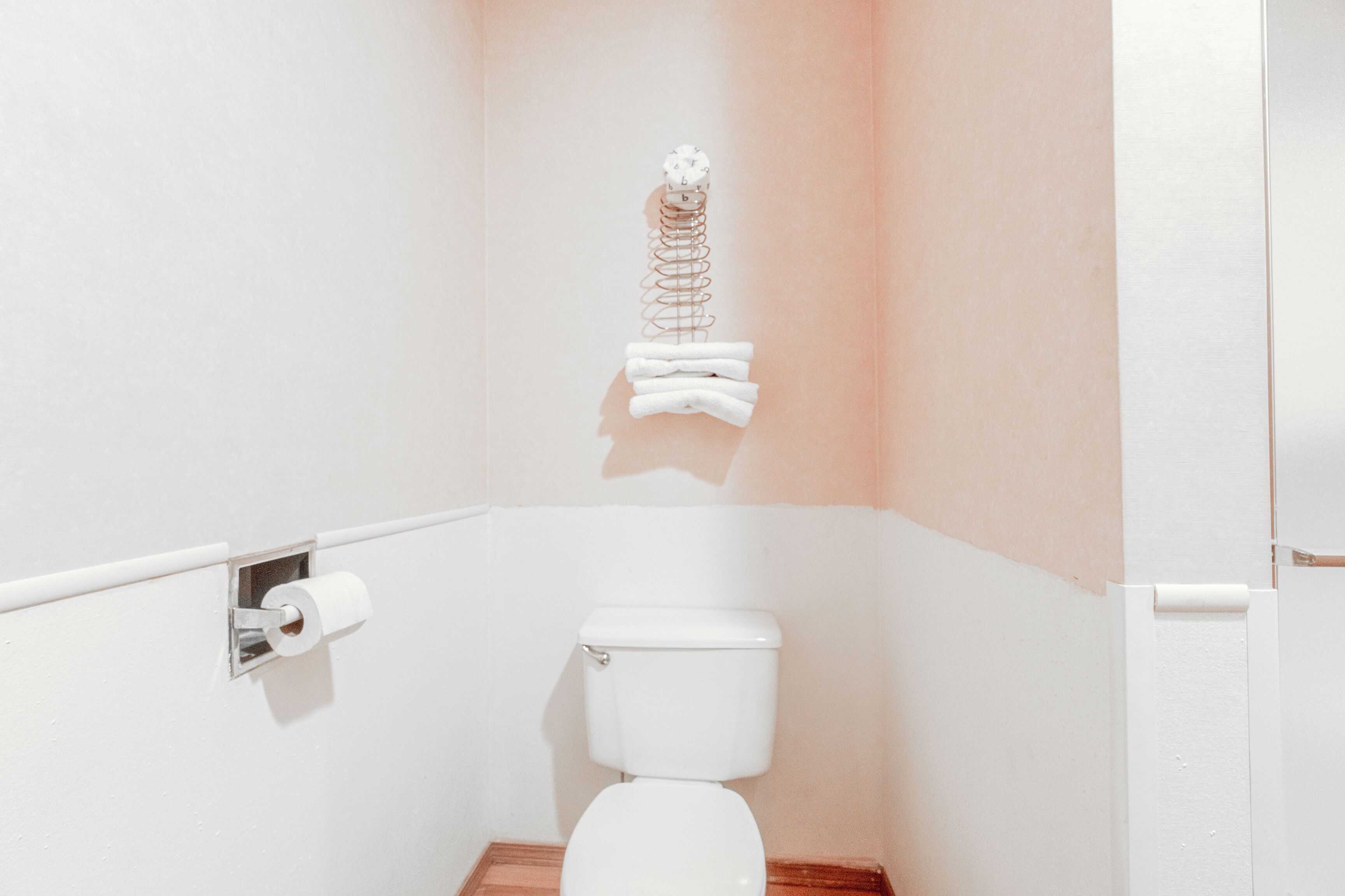 A small, white bathroom with a toilet, a paper towel dispenser, and a toilet paper holder mounted on the wall.