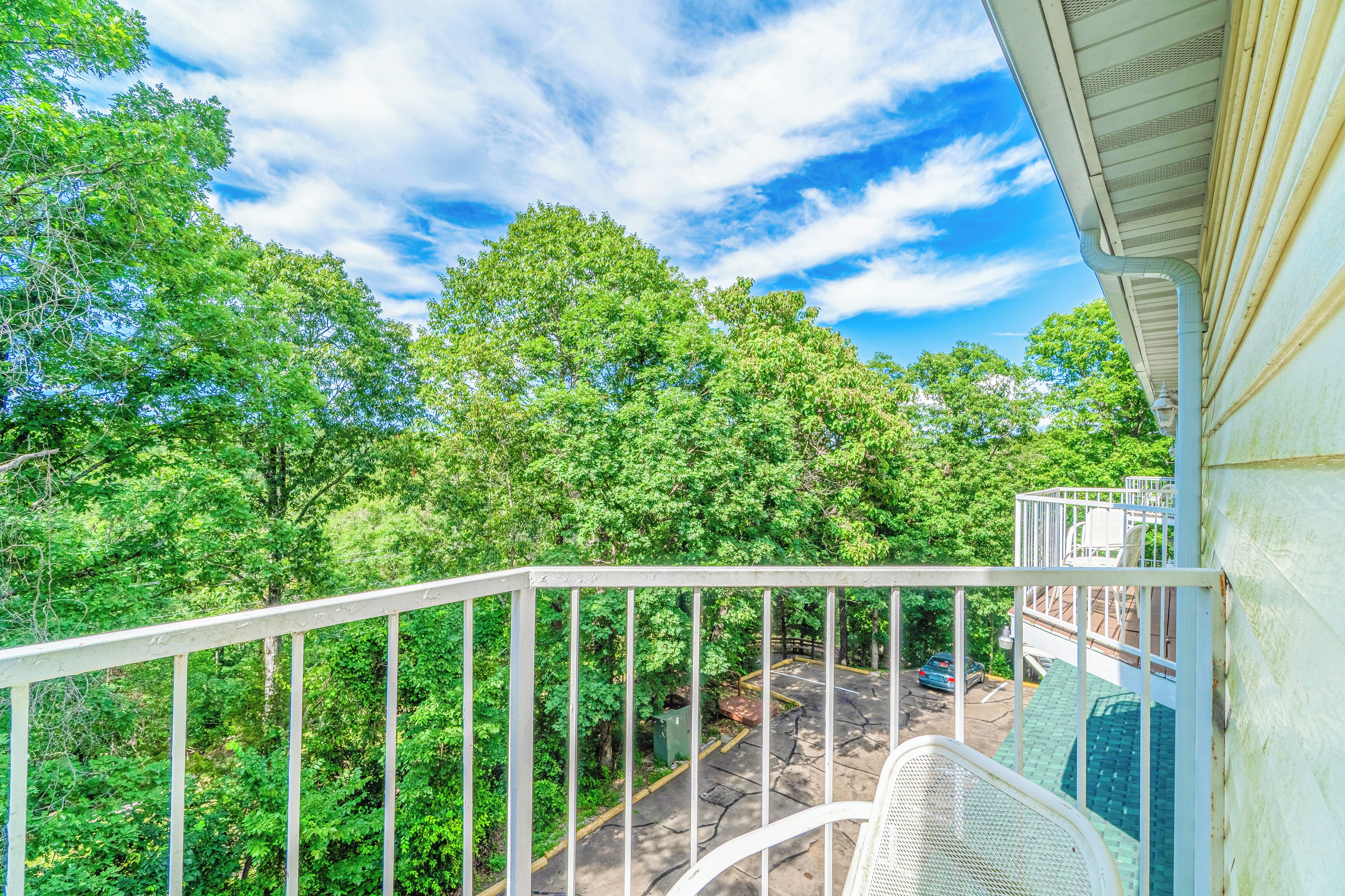 A balcony with a view of a parking area and trees.